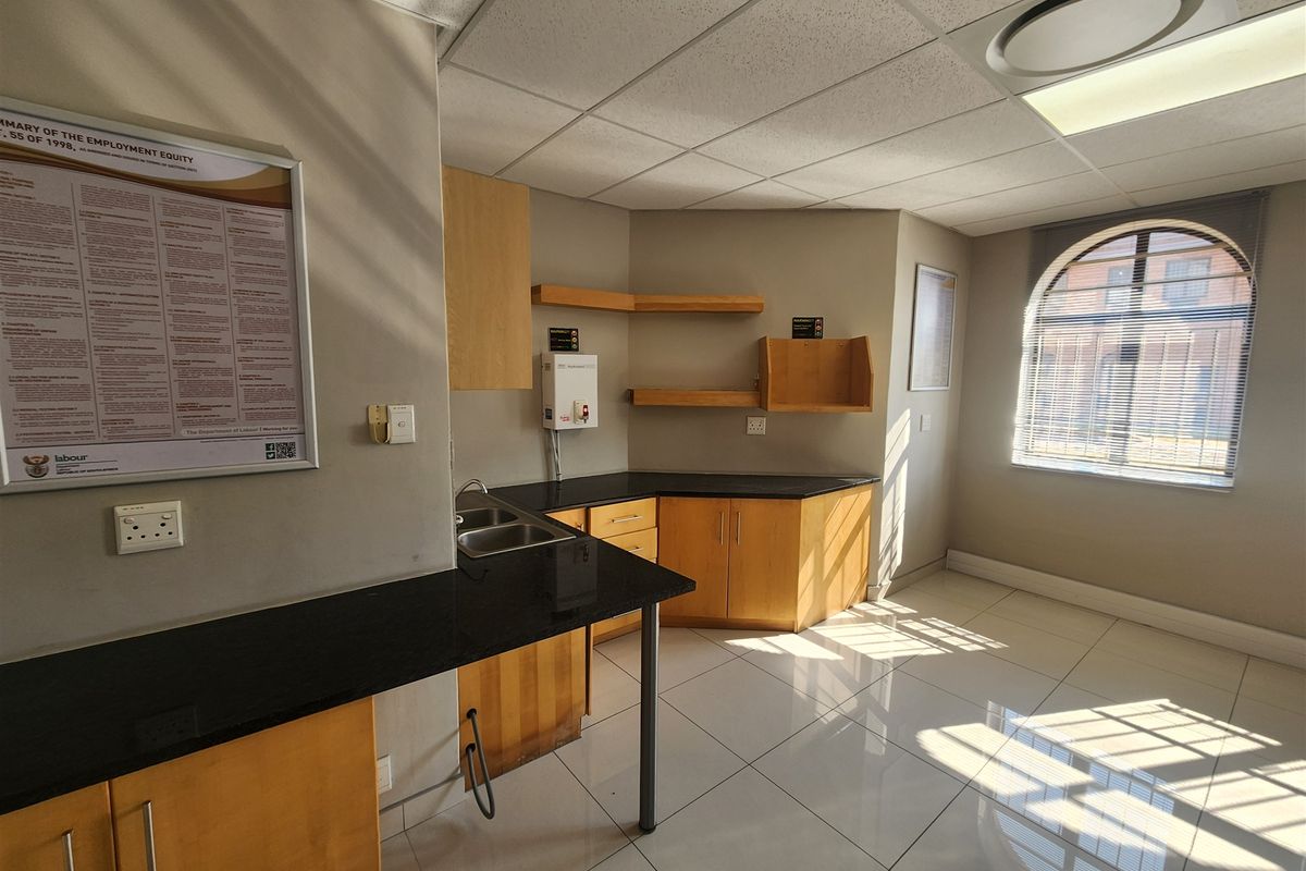A functional office kitchenette featuring light wood cabinetry, dark granite countertops, a stainless steel sink, and an arched window with blinds.