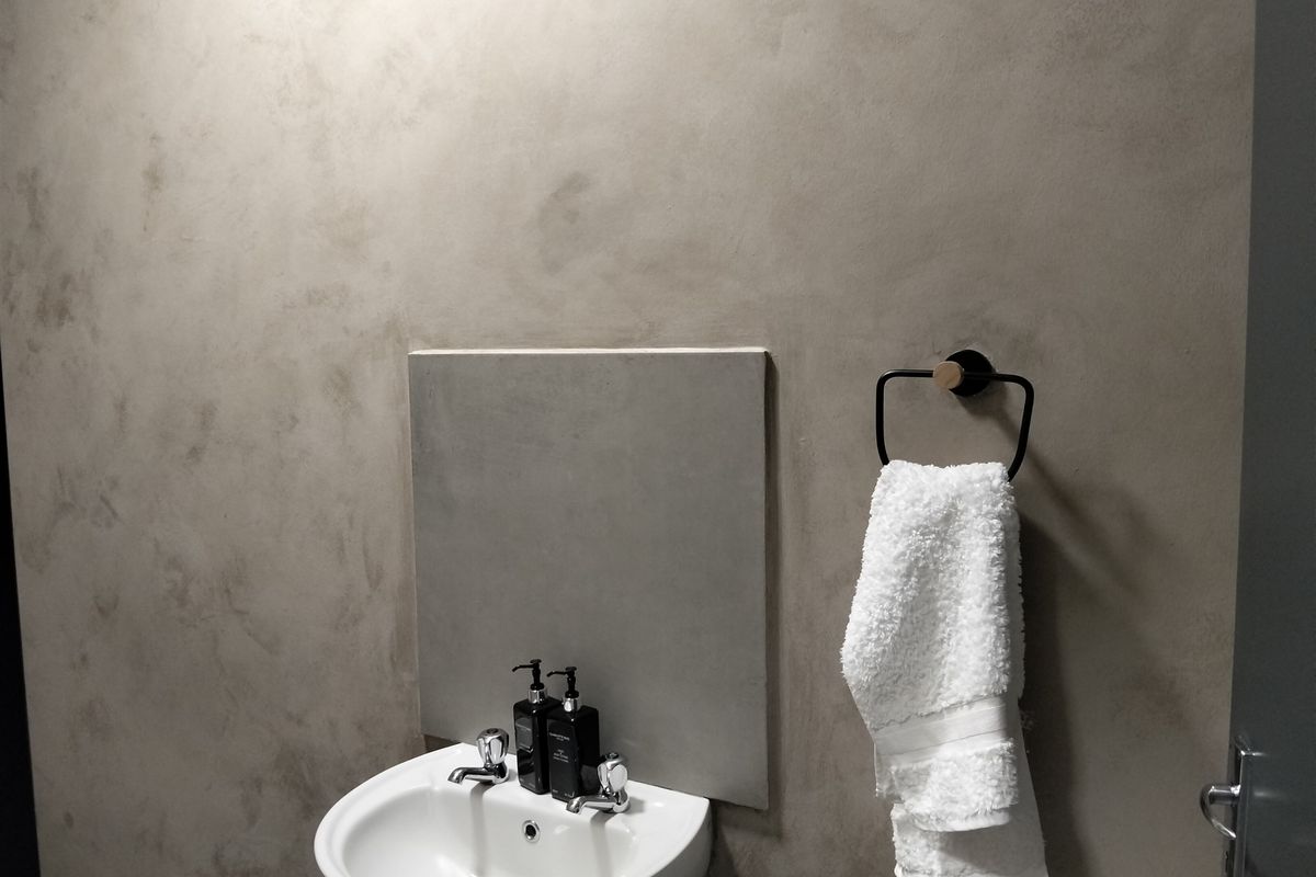 A modern bathroom featuring a wall-mounted basin with chrome taps and a minimalist square mirror against a textured concrete-effect wall finish.