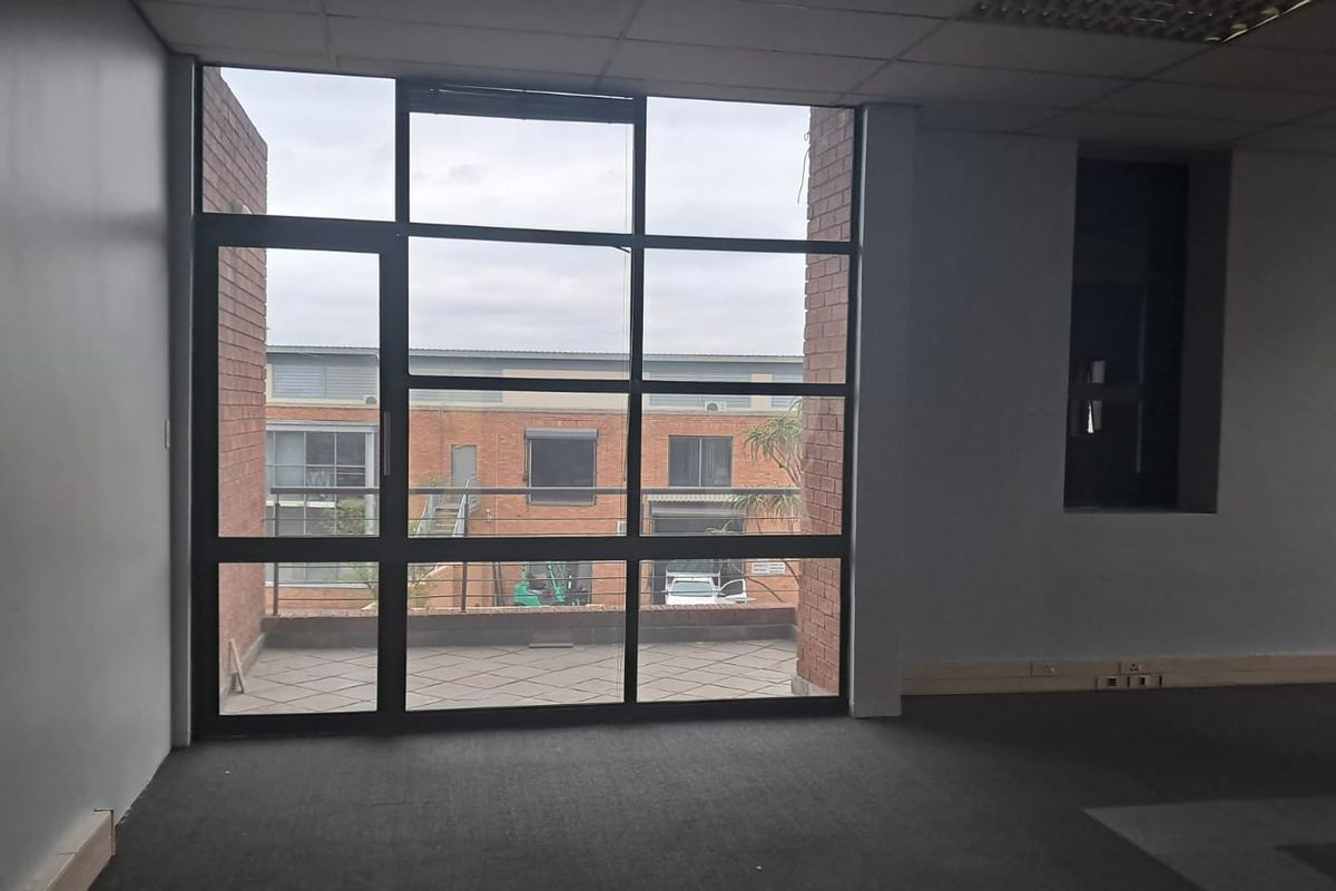 An empty office space featuring large floor-to-ceiling windows, exposed brick accents, and direct access to a private balcony area.