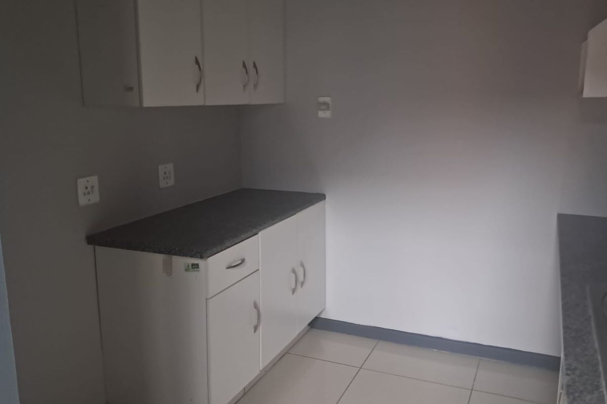 A functional kitchenette area featuring white cabinetry, stone-look countertops, and tiled flooring, suitable for office staff use.