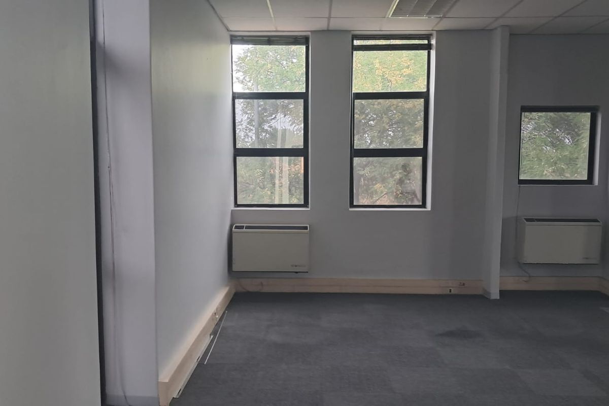 An empty office space featuring grey carpet flooring, neutral walls, and two wall-mounted HVAC units providing climate control.