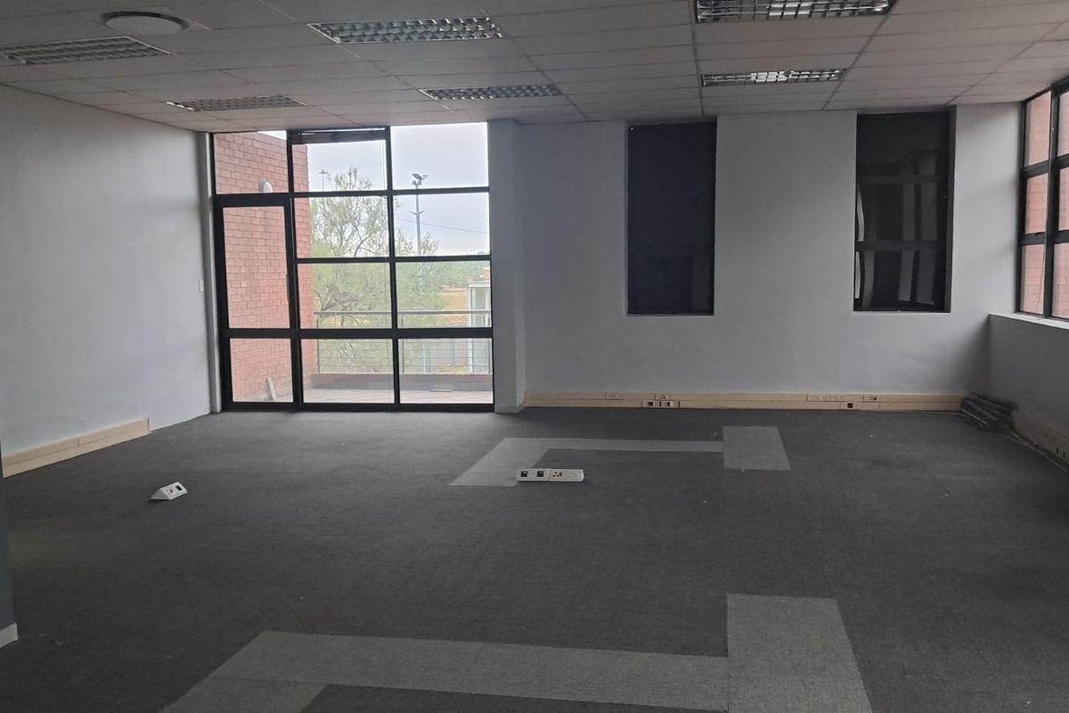 Spacious open-plan office area featuring large windows, suspended ceiling with recessed lighting, and floor-mounted power points.