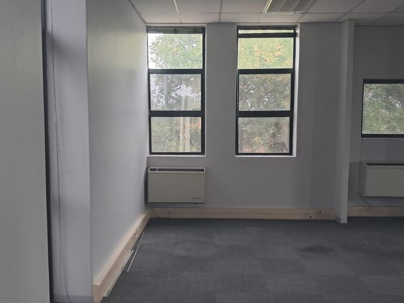 An empty office space featuring grey carpet flooring, neutral walls, and two wall-mounted HVAC units providing climate control.
