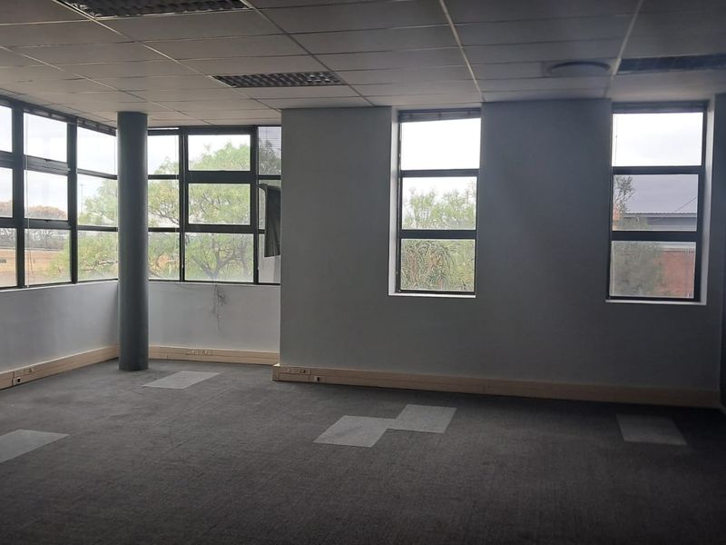 An empty, open-plan office space featuring large windows, a suspended ceiling, and grey carpeting, offering a versatile layout for professional use.