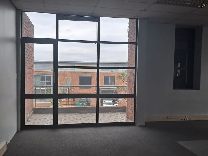 An empty office space featuring large floor-to-ceiling windows, exposed brick accents, and direct access to a private balcony area.