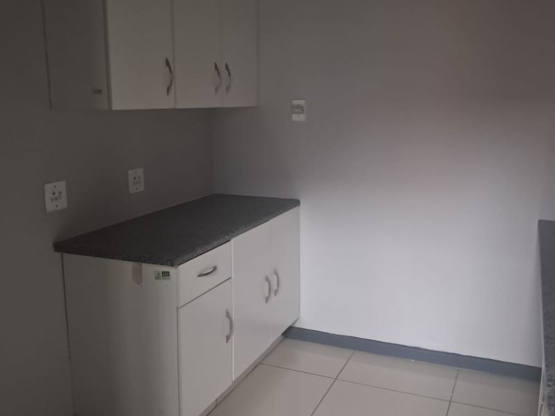 A functional kitchenette area featuring white cabinetry, stone-look countertops, and tiled flooring, suitable for office staff use.
