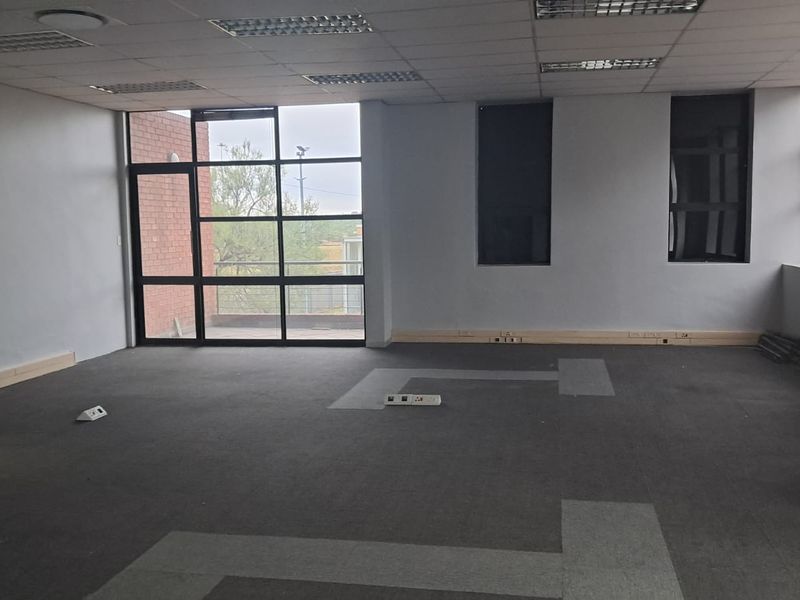 Spacious open-plan office area featuring large windows, suspended ceiling with recessed lighting, and floor-mounted power points.