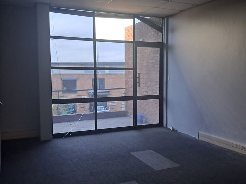 An empty office space featuring large floor-to-ceiling windows, carpeted flooring, and direct access to an outdoor balcony area.