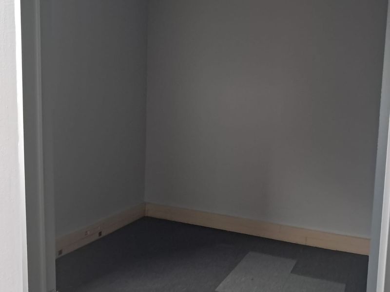 A small, empty office or utility space featuring grey walls, unfinished timber skirting boards, and grey floor tiles.