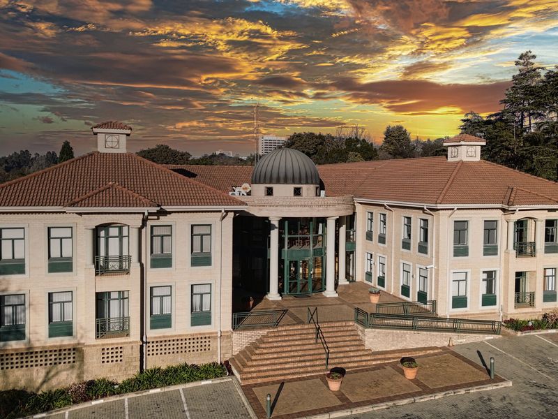 Aerial view of a professional office building featuring a central dome, terracotta roof, and paved parking area at sunset.