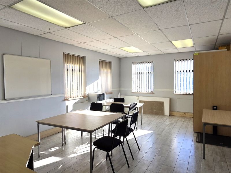 A functional office space featuring tiled flooring, suspended ceiling with recessed lighting, and multiple windows with vertical blinds.