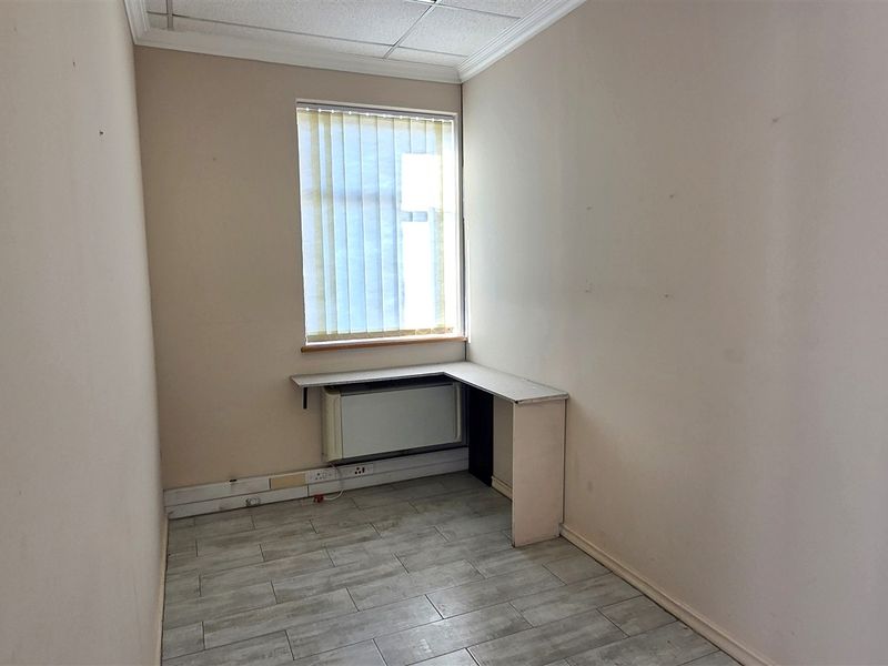 A compact, empty office space featuring tiled flooring, a built-in desk, and vertical window blinds, ready for professional use.