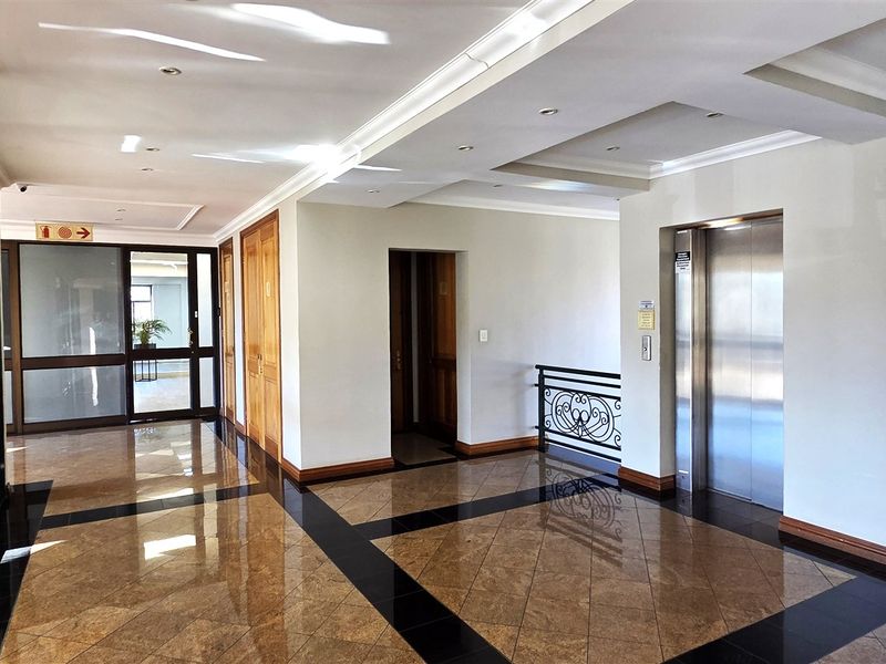 A spacious, well-maintained office building lobby featuring polished granite flooring, recessed ceiling lighting, and a modern stainless steel elevator.