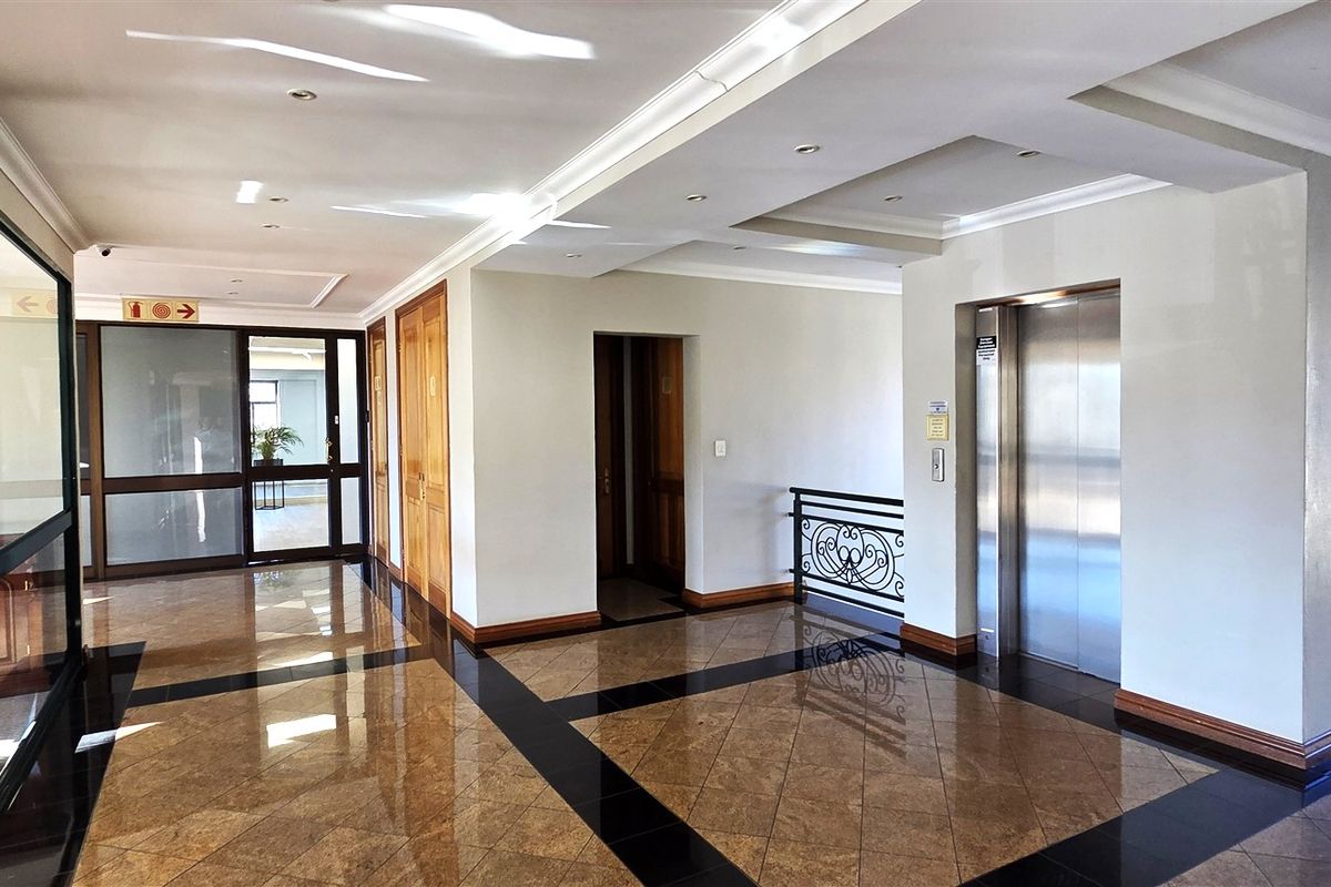 A spacious, well-maintained office building lobby featuring polished granite flooring, recessed ceiling lighting, and a modern stainless steel elevator.