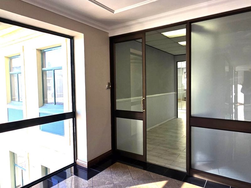 A bright, professional office space featuring modern frosted glass partitions, tiled flooring, and large windows providing ample natural light.