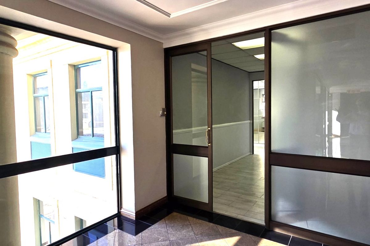A bright, professional office space featuring modern frosted glass partitions, tiled flooring, and large windows providing ample natural light.