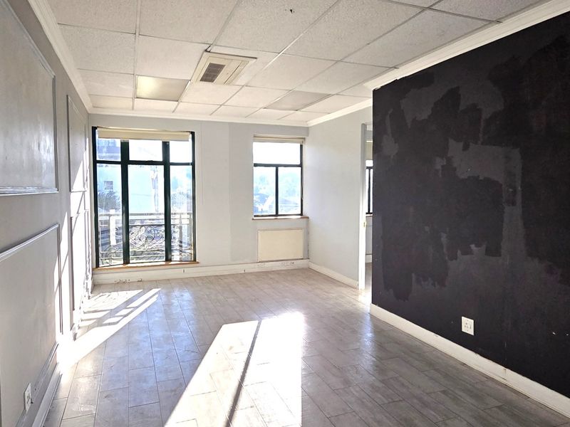 An empty office space featuring tiled flooring, a suspended ceiling, and large windows providing natural light, with a prominent feature wall requiring cosmetic attention.
