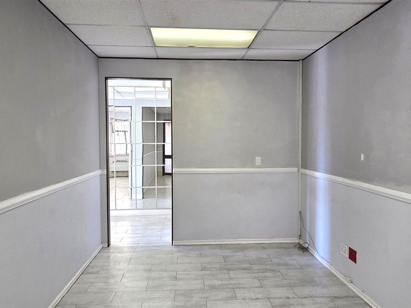 A vacant office space featuring a drop ceiling, recessed lighting, chair rail molding, and tiled flooring, ready for customization.
