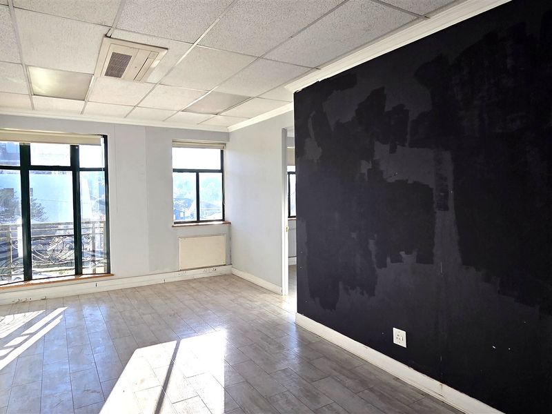 An empty office space featuring laminate flooring, a suspended ceiling with integrated air conditioning, and large windows providing natural light.