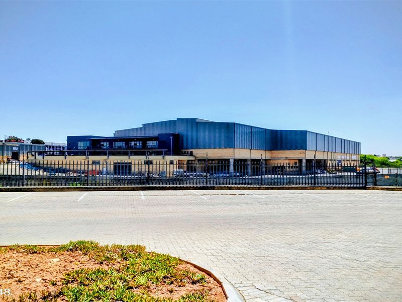 A wide-angle view of an industrial property featuring a large paved parking area, secure perimeter fencing, and a modern metal-clad building structure.