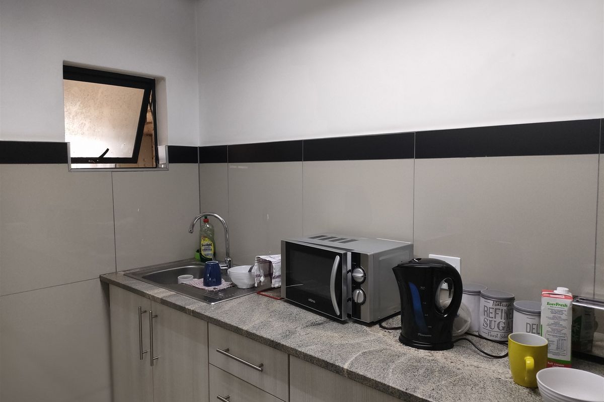 A functional kitchenette featuring granite countertops, built-in cabinetry, a stainless steel sink, and a tiled backsplash.