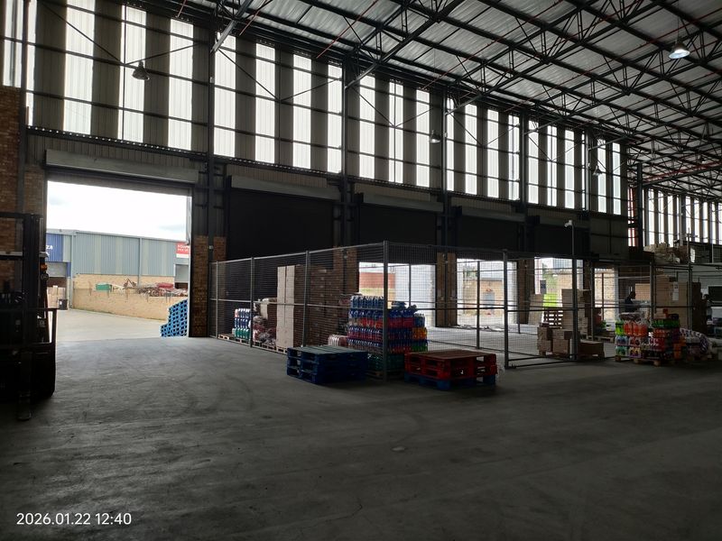 Spacious industrial warehouse area featuring high ceilings with exposed steel trusses, concrete flooring, and secure wire mesh partitioning for storage.