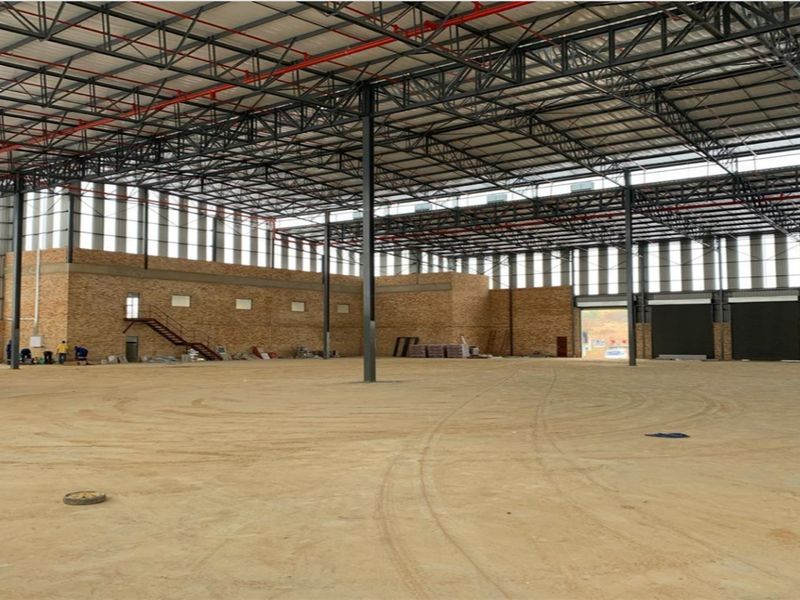 Large industrial warehouse space featuring high exposed steel trusses, fire sprinkler system, roller shutter doors, and durable face brick wall construction.