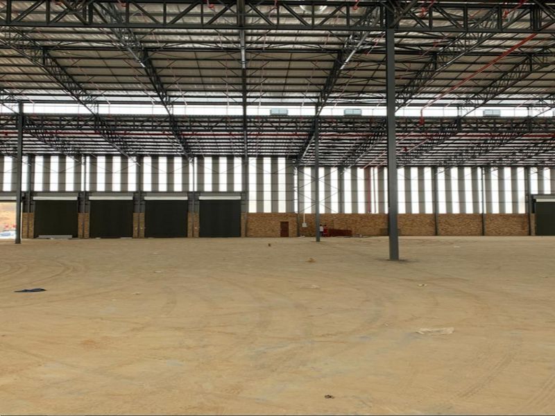 A large, open-plan industrial warehouse space featuring high-clearance steel truss roofing, fire sprinkler systems, and multiple roller shutter doors for logistics access.