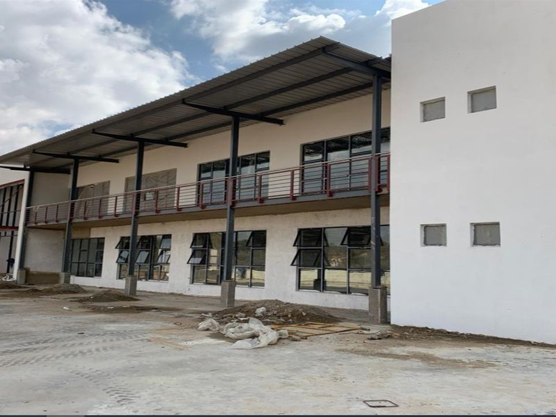 Rear view of a modern industrial building featuring a covered balcony, steel structural elements, and large aluminium-framed windows with an unfinished exterior ground area.