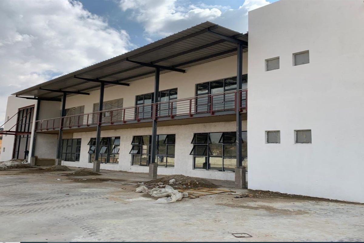Rear view of a modern industrial building featuring a covered balcony, steel structural elements, and large aluminium-framed windows with an unfinished exterior ground area.
