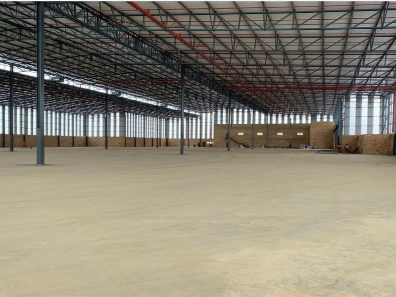 Expansive industrial warehouse space featuring high steel truss ceilings, concrete flooring, and robust steel support columns, suitable for large-scale storage or manufacturing operations.