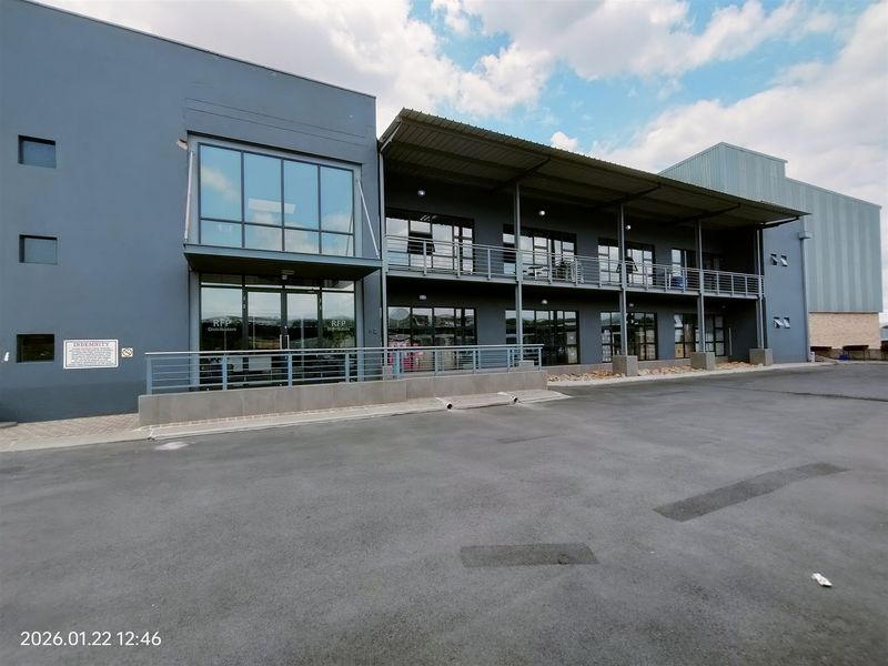 Modern industrial facility featuring a multi-level facade with glass curtain walls, steel balcony structures, and a paved asphalt forecourt.