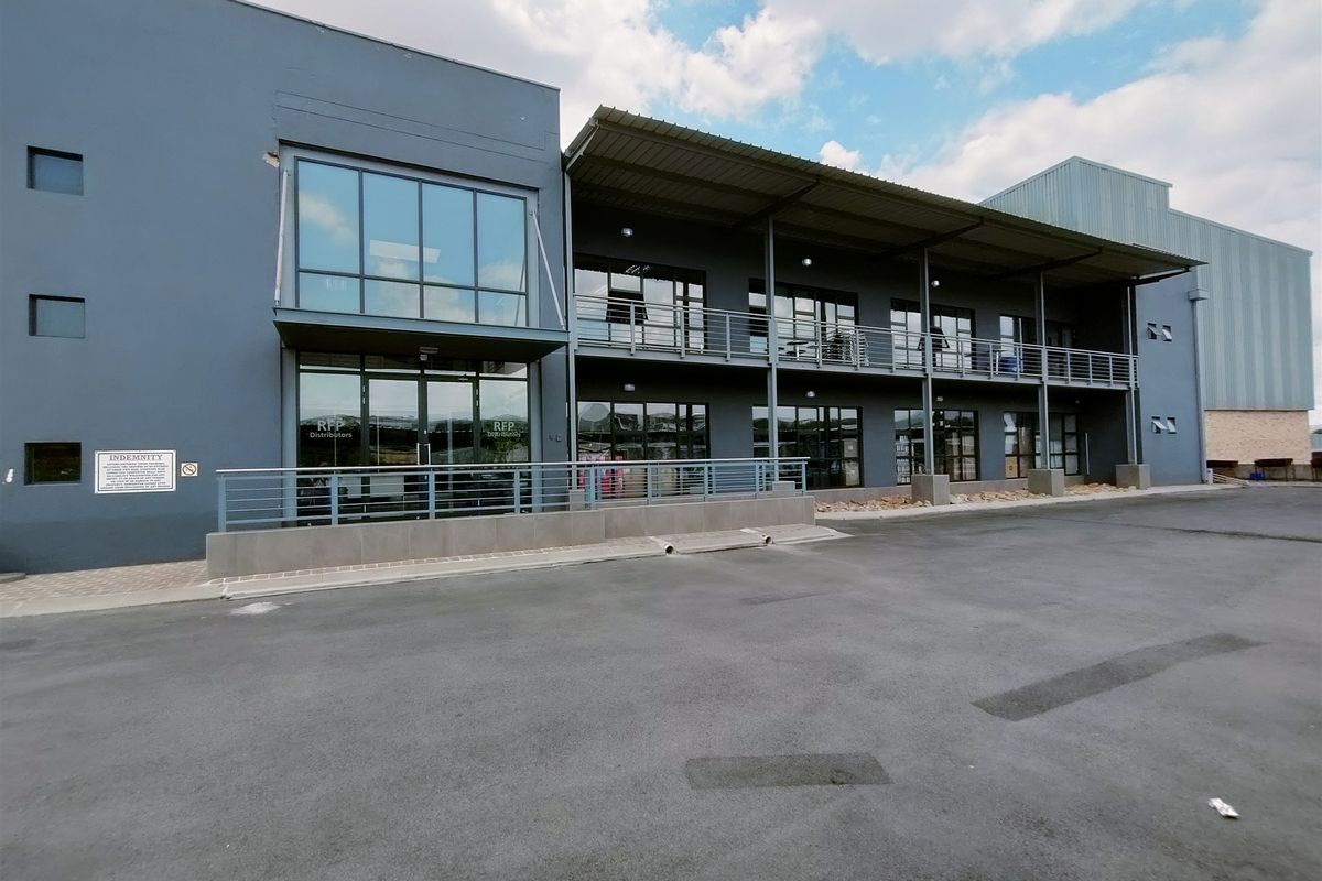 Modern industrial facility featuring a multi-level facade with glass curtain walls, steel balcony structures, and a paved asphalt forecourt.