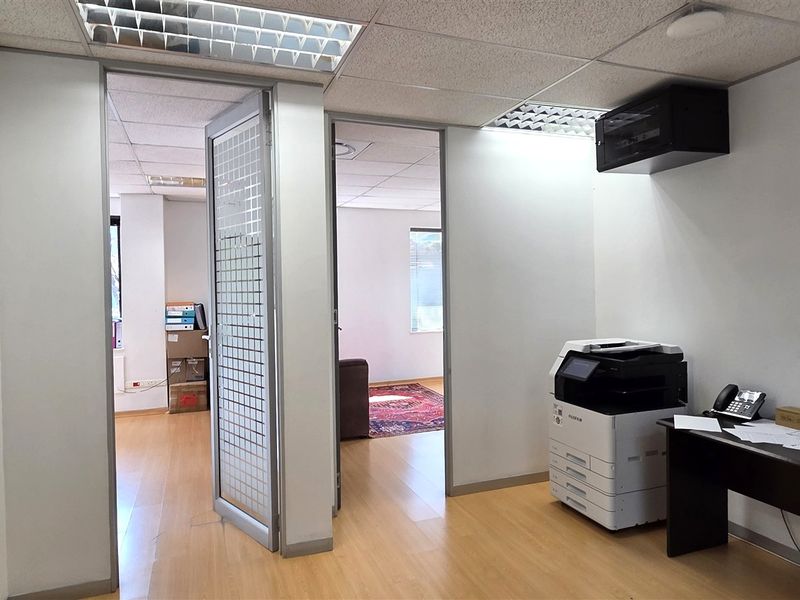 A functional office space featuring laminate flooring, suspended ceilings with recessed lighting, and multiple glass-panelled doors providing access to adjacent work areas.