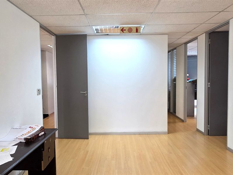 A bright, empty office space featuring laminate flooring, a suspended ceiling, and glass partition walls, providing a clean and professional work environment.