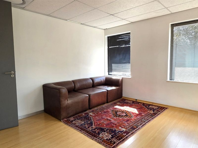 A functional office space featuring laminate flooring, a suspended ceiling, and dual windows with fitted venetian blinds.