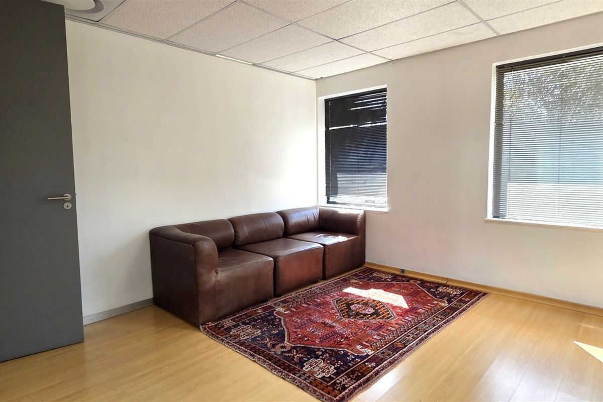 A functional office space featuring laminate flooring, a suspended ceiling, and dual windows with fitted venetian blinds.