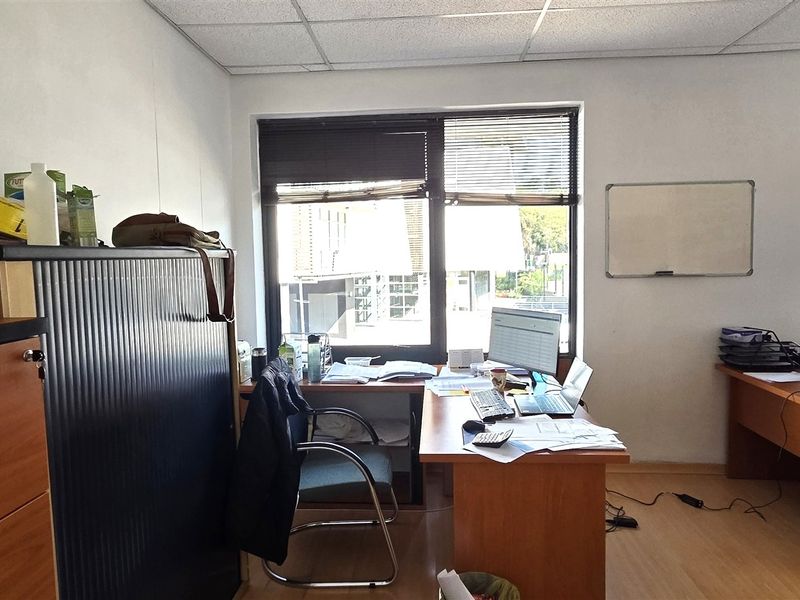 A functional office space featuring laminate flooring, suspended ceiling tiles, and large windows with venetian blinds, providing natural light for a productive work environment.