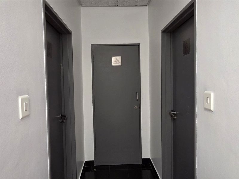 A clean, well-maintained office hallway featuring grey internal doors, tiled flooring, and a drop ceiling.