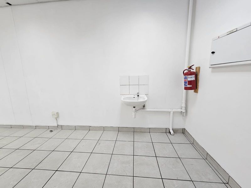 A functional utility space featuring tiled flooring, a wall-mounted basin with tiled splashback, and essential safety equipment including a fire extinguisher.