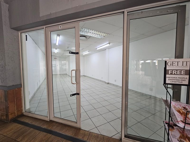 Empty retail storefront unit featuring glass entrance doors, tiled flooring, and overhead fluorescent lighting, suitable for various commercial business applications.