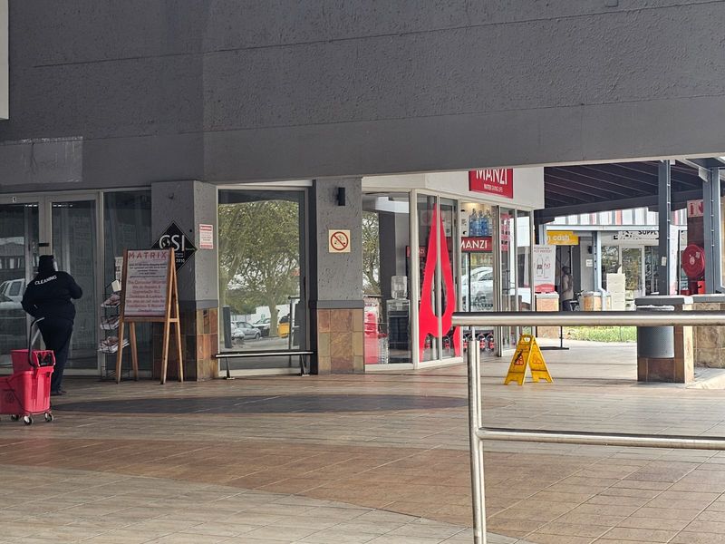 Exterior view of a retail shopping center storefront with glass display windows, tiled walkway, and stone cladding accents.