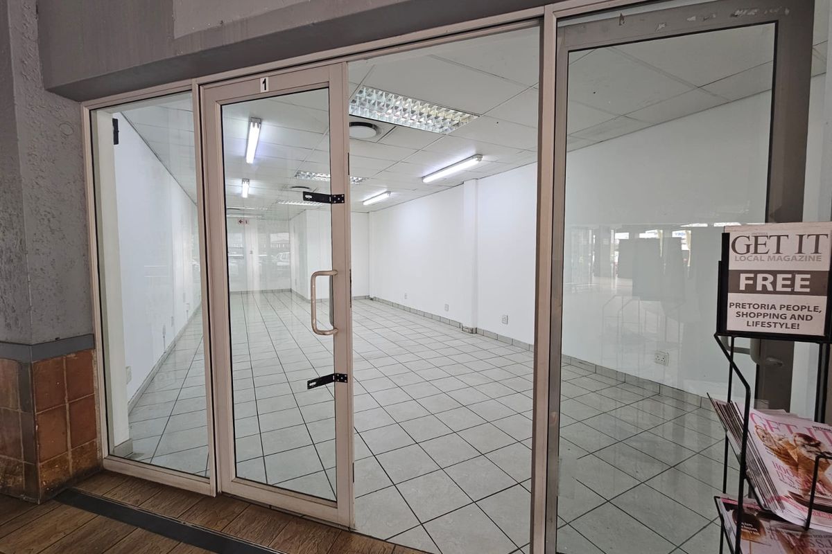 Empty retail storefront unit featuring glass entrance doors, tiled flooring, and overhead fluorescent lighting, suitable for various commercial business applications.