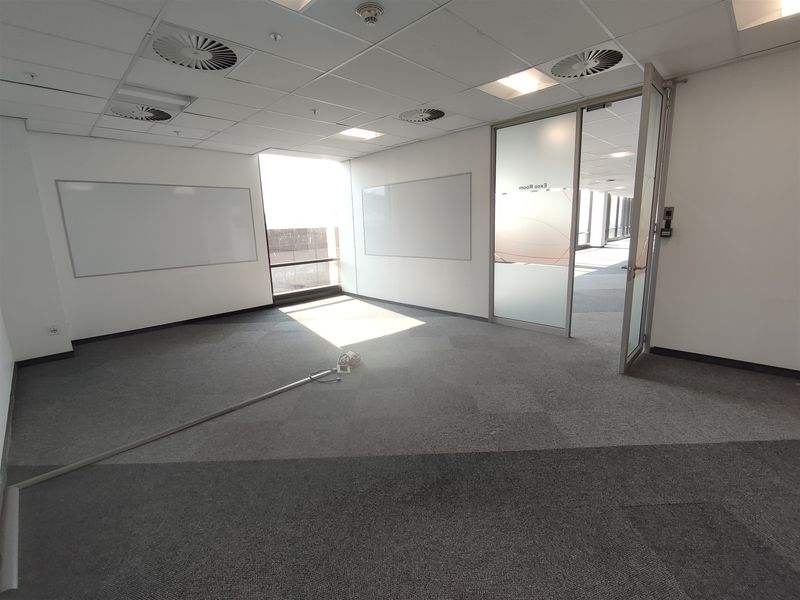 A vacant office space featuring a glass partition, wall-mounted whiteboards, suspended ceiling with recessed lighting, and carpeted flooring.
