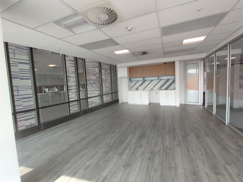 A bright, modern office space featuring laminate flooring, built-in cabinetry, glass partitions, and a suspended ceiling with integrated lighting and air conditioning.