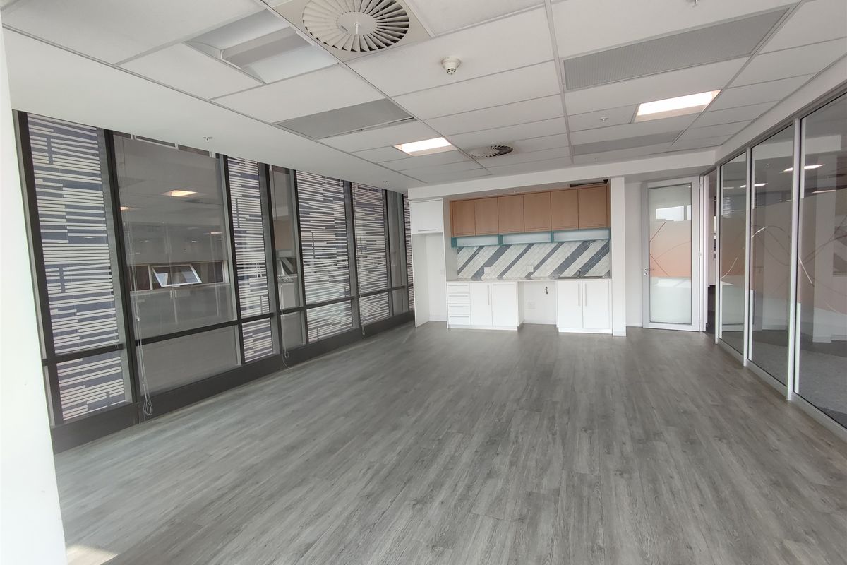 A bright, modern office space featuring laminate flooring, built-in cabinetry, glass partitions, and a suspended ceiling with integrated lighting and air conditioning.
