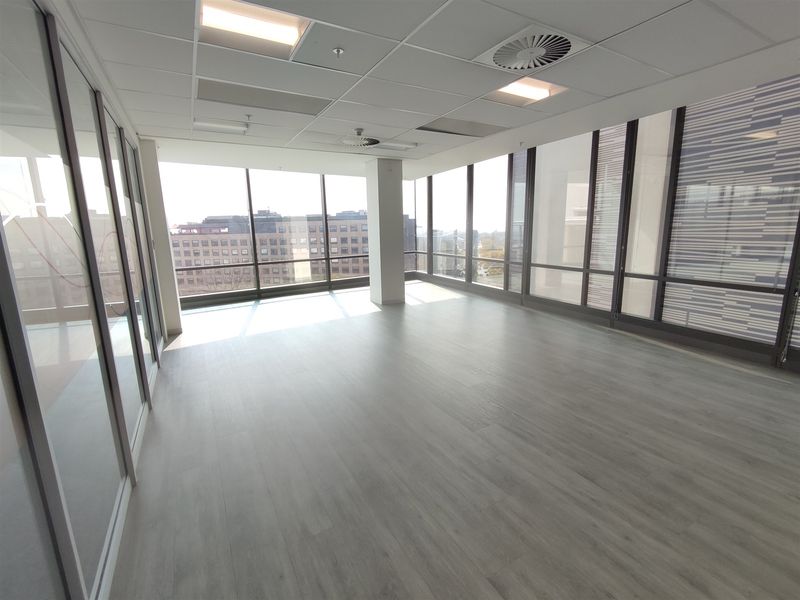 A bright, modern, empty office space featuring floor-to-ceiling windows, glass partitions, and a suspended ceiling with integrated lighting.