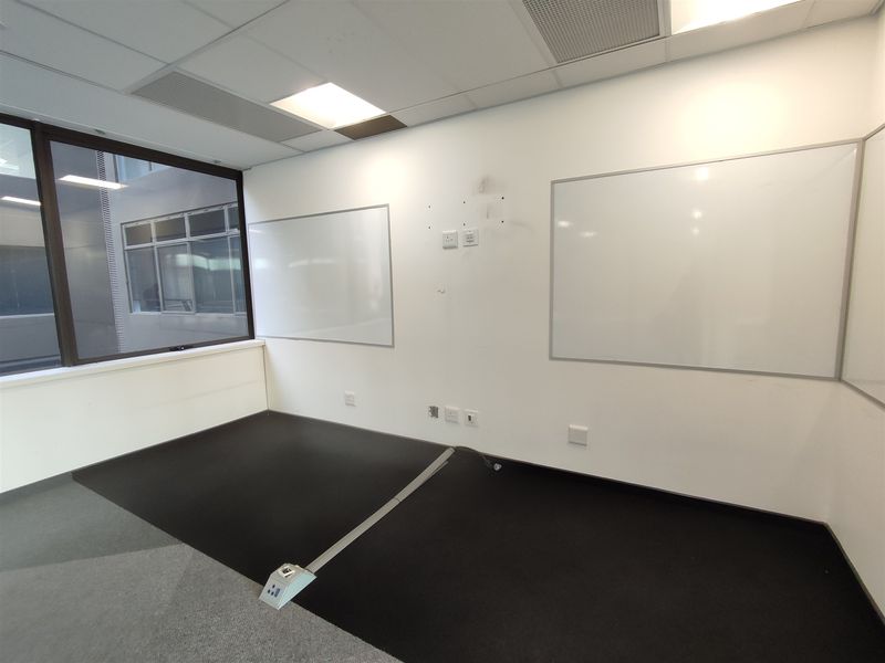 A vacant office space featuring a suspended ceiling, large window, wall-mounted whiteboards, and integrated floor power connectivity.