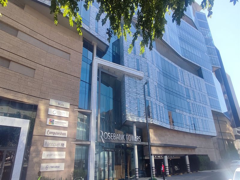 Modern commercial office building facade featuring glass curtain walls, stone cladding, and a prominent entrance with tenant signage.