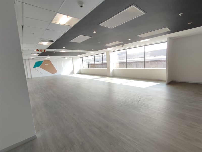 Spacious, open-plan office area featuring modern laminate flooring, suspended ceilings with recessed lighting, and large windows providing ample natural light.